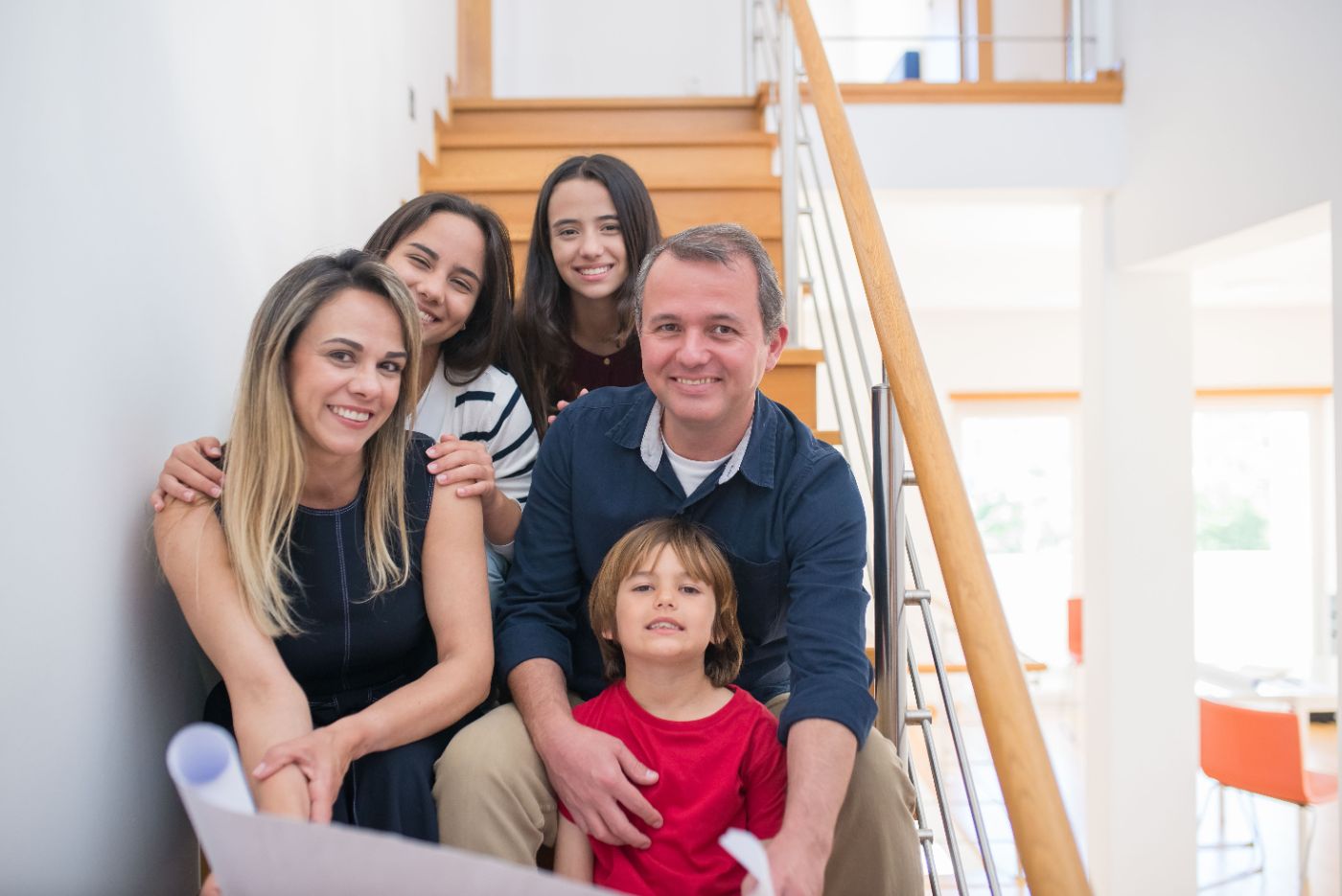 A smiling family of five sitting together on the stairs at home