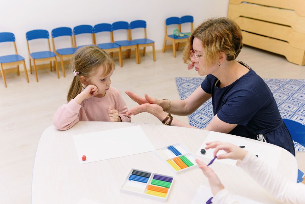 A therapist working with a young girl at a table with modeling clay